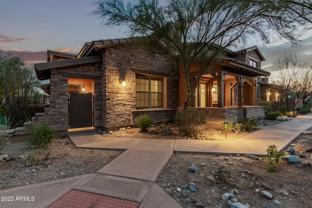 view of front of home featuring covered porch, a tile roof, and stone siding