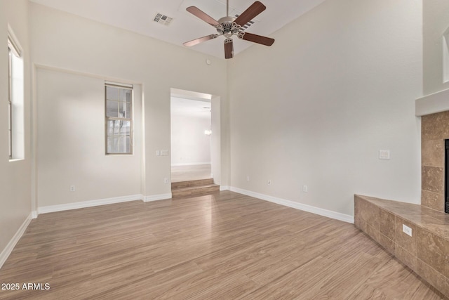 unfurnished living room featuring light wood-type flooring, a tile fireplace, visible vents, and a ceiling fan