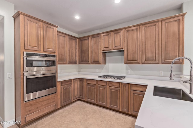 kitchen with brown cabinets, recessed lighting, appliances with stainless steel finishes, a sink, and light stone countertops