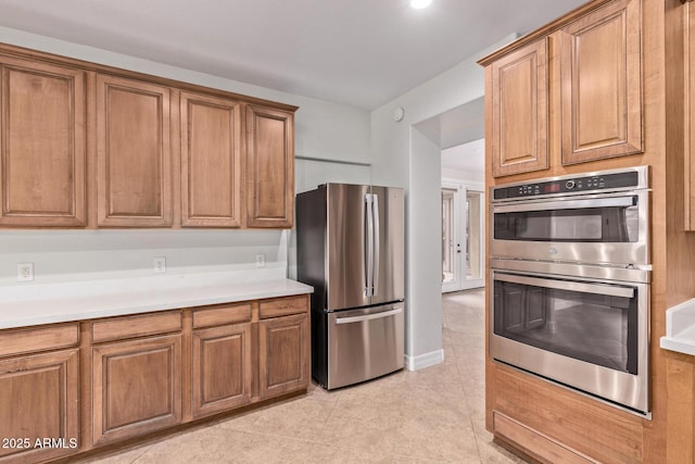 kitchen with appliances with stainless steel finishes, light countertops, brown cabinetry, and light tile patterned floors