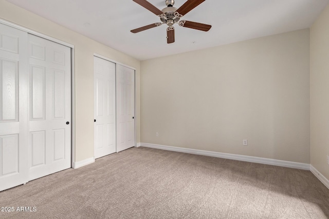 unfurnished bedroom featuring carpet floors, a ceiling fan, baseboards, and two closets