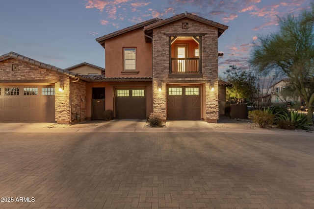 view of front facade with driveway, stone siding, a tiled roof, and stucco siding