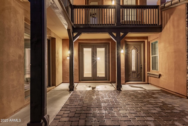 entrance to property with french doors, a balcony, and stucco siding