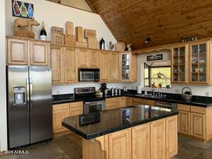 kitchen featuring a kitchen island, appliances with stainless steel finishes, glass insert cabinets, vaulted ceiling, and wooden ceiling