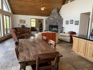 dining area featuring wood ceiling, a stone fireplace, and high vaulted ceiling