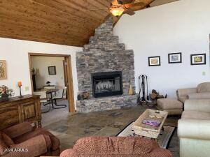 living area with a fireplace, a ceiling fan, wooden ceiling, and vaulted ceiling