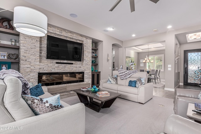 living room with built in shelves, light tile patterned floors, a fireplace, and ceiling fan with notable chandelier