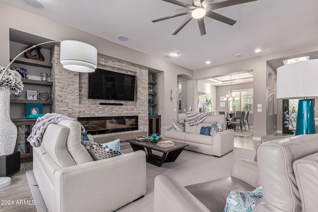 living room with built in features, light hardwood / wood-style flooring, a stone fireplace, and ceiling fan