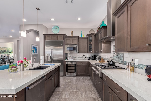 kitchen featuring backsplash, wall chimney exhaust hood, beverage cooler, built in appliances, and decorative light fixtures