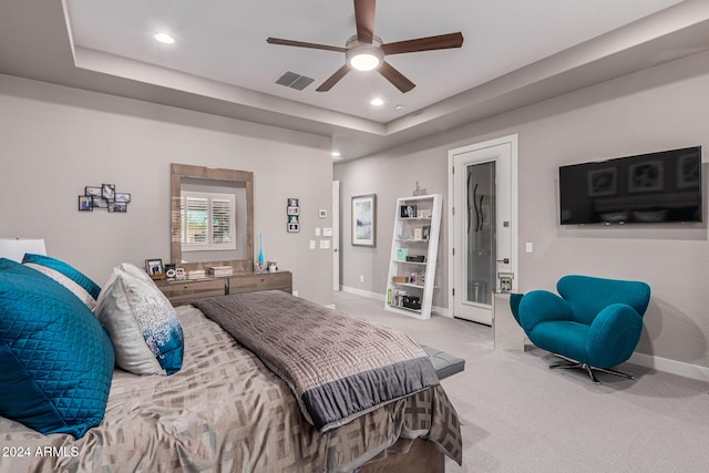 bedroom with ceiling fan, light colored carpet, and a tray ceiling