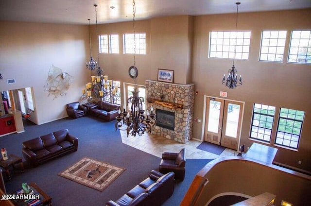 living room with a notable chandelier, a stone fireplace, french doors, and a towering ceiling