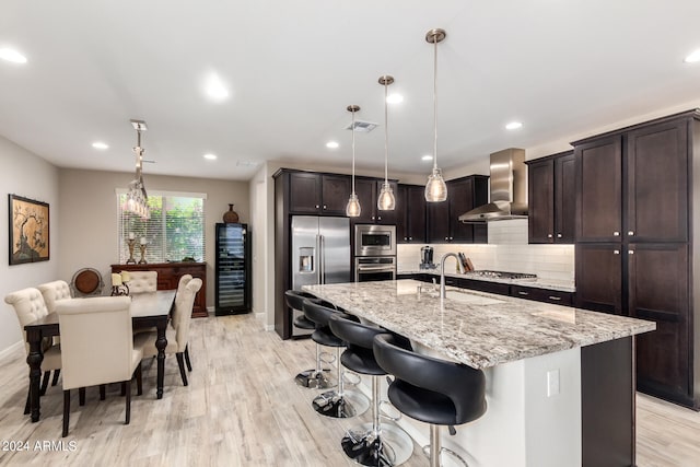 kitchen with pendant lighting, backsplash, wall chimney exhaust hood, sink, and appliances with stainless steel finishes