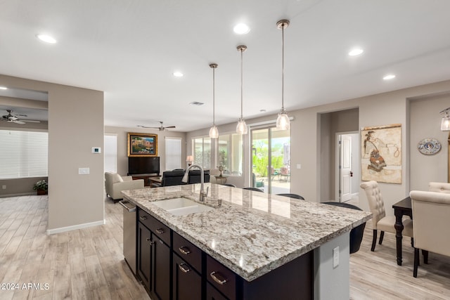 kitchen with ceiling fan, light hardwood / wood-style flooring, hanging light fixtures, sink, and a kitchen island with sink