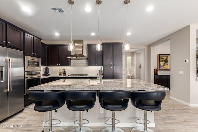 kitchen featuring wall chimney exhaust hood, light wood-type flooring, decorative light fixtures, and appliances with stainless steel finishes