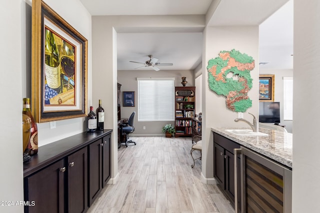 bar with dark brown cabinets, ceiling fan, light hardwood / wood-style floors, beverage cooler, and sink