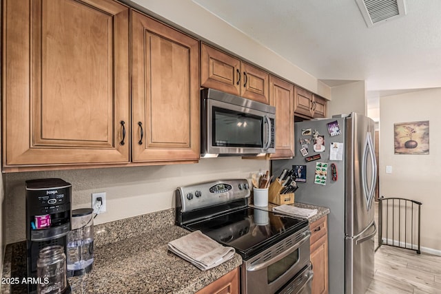 6133 E Saddleback St, Mesa, AZ 85215 - kitchen featuring stainless steel appliances, brown cabinetry, light wood finished floors, and dark stone countertops