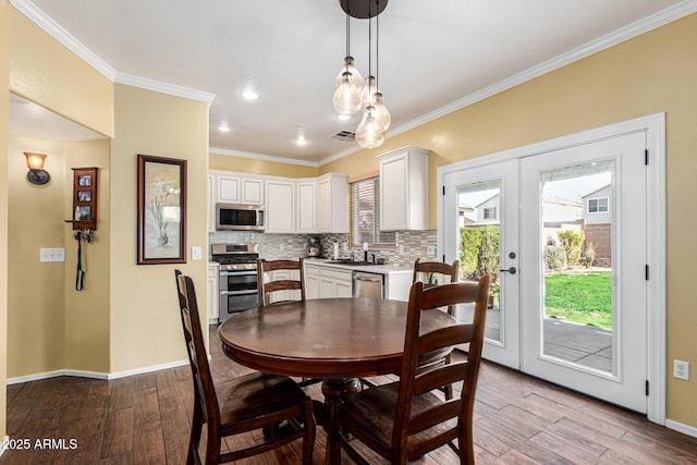 dining space featuring sink, light wood-type flooring, crown molding, and french doors