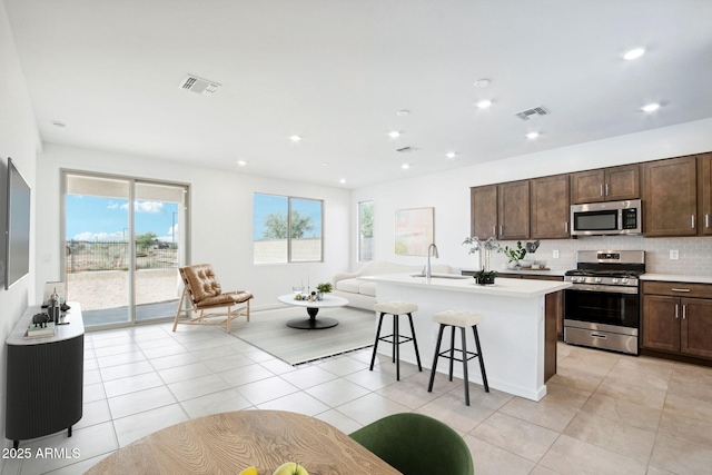 kitchen with visible vents, light tile patterned flooring, open floor plan, an island with sink, and appliances with stainless steel finishes
