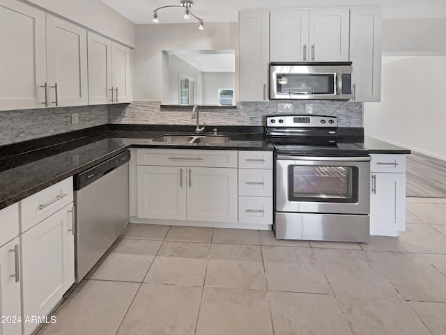 kitchen with appliances with stainless steel finishes, sink, light tile patterned floors, dark stone countertops, and white cabinetry