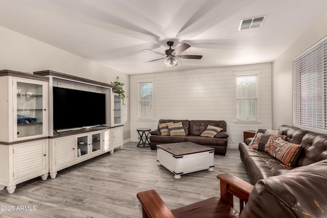 living room featuring light hardwood / wood-style flooring, wooden walls, and ceiling fan