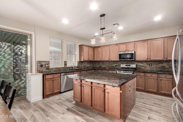 kitchen featuring a center island, stainless steel appliances, sink, dark stone counters, and pendant lighting