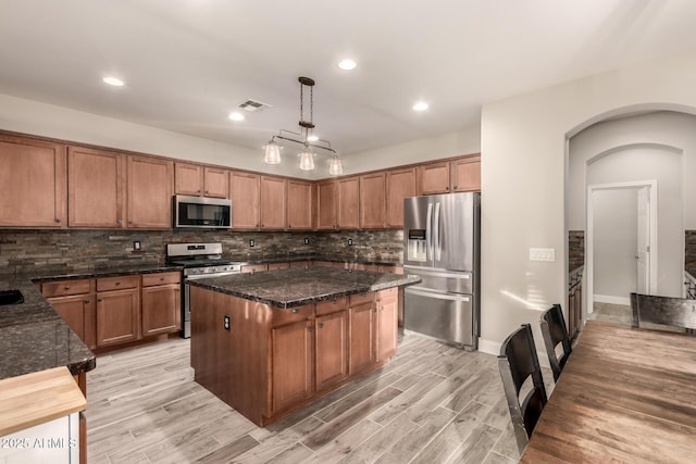 kitchen with light wood-type flooring, a center island, backsplash, appliances with stainless steel finishes, and pendant lighting