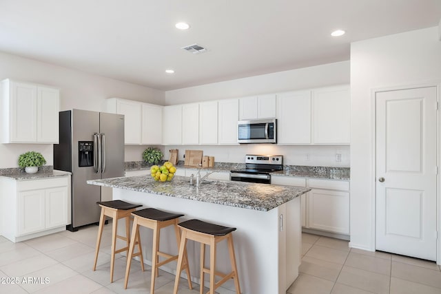 kitchen featuring stone counters, white cabinets, light tile patterned floors, stainless steel appliances, and a center island with sink