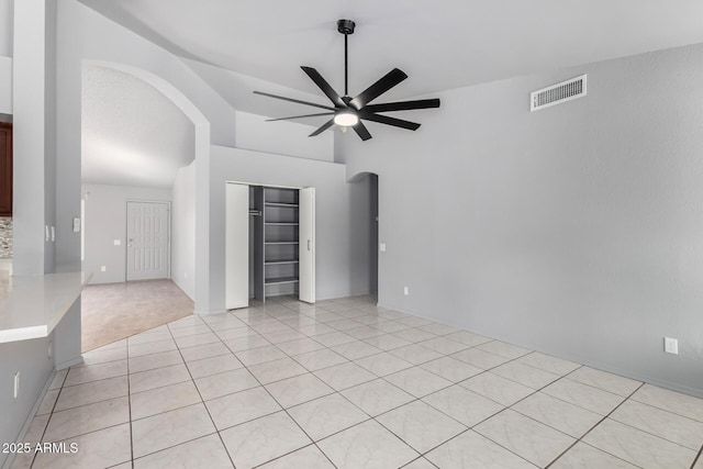 spare room featuring arched walkways, light tile patterned floors, visible vents, a ceiling fan, and vaulted ceiling