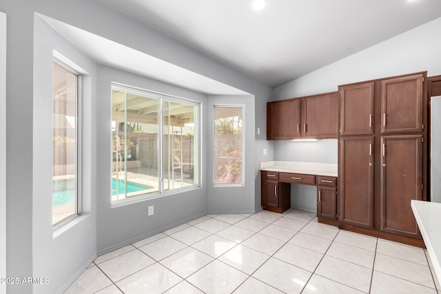 kitchen featuring baseboards, lofted ceiling, light countertops, built in desk, and light tile patterned flooring