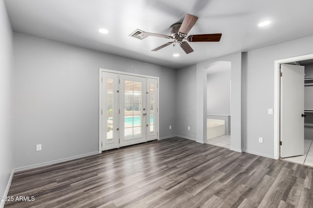 empty room with baseboards, arched walkways, a ceiling fan, wood finished floors, and recessed lighting