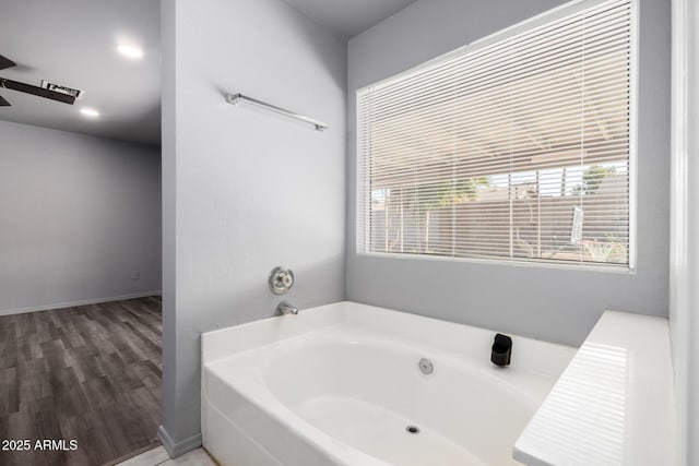 bathroom featuring wood finished floors, baseboards, and a bath