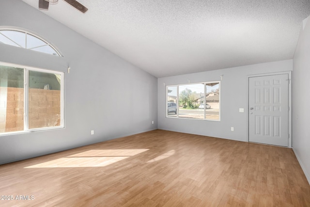 empty room with ceiling fan, vaulted ceiling, a textured ceiling, and wood finished floors