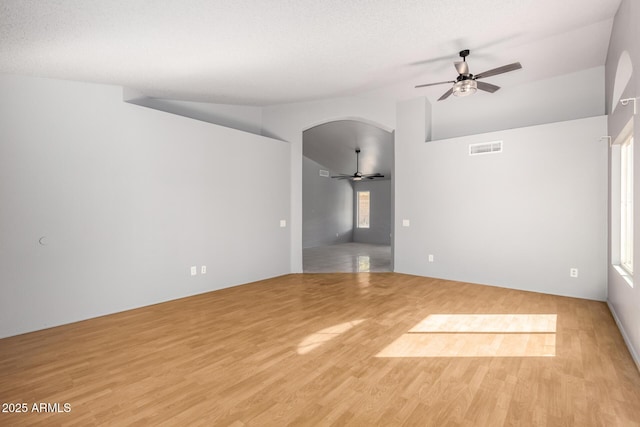 empty room with visible vents, arched walkways, a ceiling fan, lofted ceiling, and light wood-type flooring