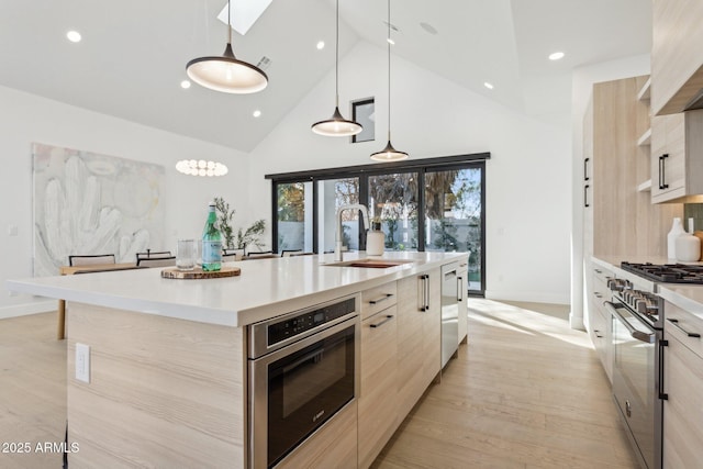 kitchen with light hardwood / wood-style flooring, stainless steel range, an island with sink, decorative light fixtures, and oven