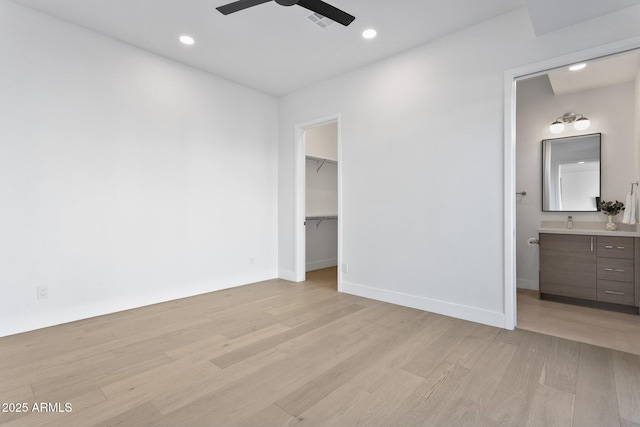 unfurnished bedroom featuring ensuite bath, a spacious closet, ceiling fan, light wood-type flooring, and a closet