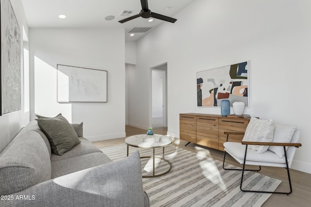 living room with ceiling fan, a towering ceiling, and light wood-type flooring