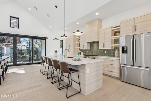 kitchen with an island with sink, stainless steel fridge, light brown cabinetry, and light hardwood / wood-style floors