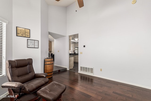 sitting room featuring baseboards, visible vents, a ceiling fan, dark wood-type flooring, and a high ceiling