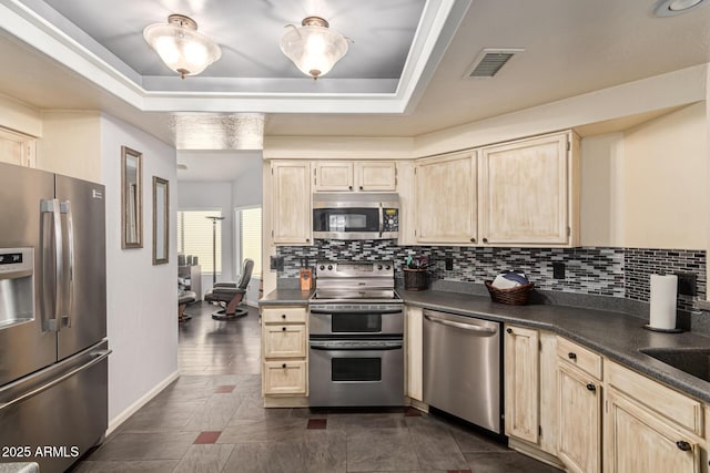 kitchen with a tray ceiling, appliances with stainless steel finishes, and dark countertops