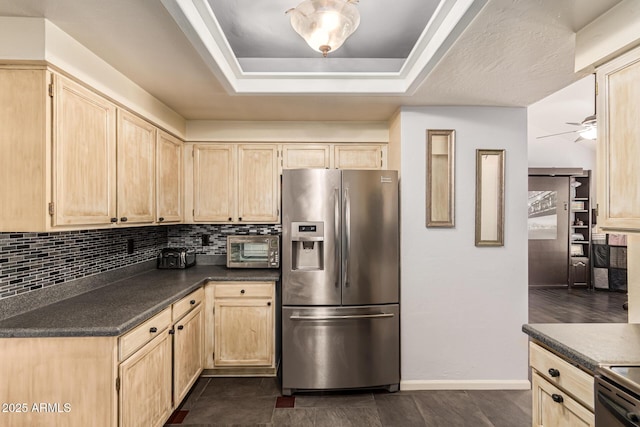 kitchen with light brown cabinets, stainless steel refrigerator with ice dispenser, a tray ceiling, dark countertops, and tasteful backsplash