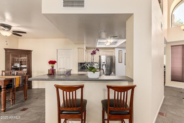 kitchen featuring dark countertops, a peninsula, stainless steel refrigerator with ice dispenser, and visible vents