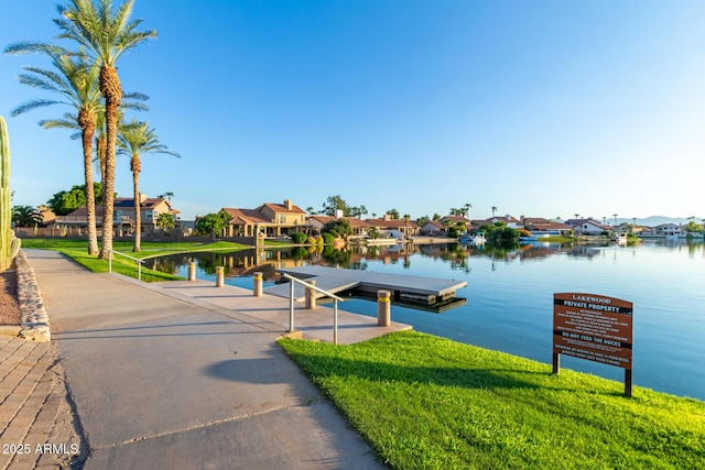 dock area with a water view, a residential view, and a lawn