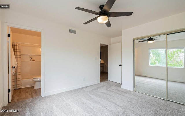 unfurnished bedroom featuring a closet, ensuite bathroom, light colored carpet, and ceiling fan