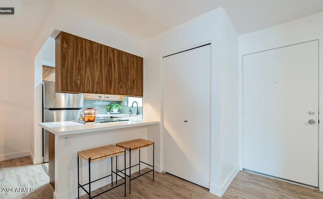 kitchen featuring light hardwood / wood-style flooring, kitchen peninsula, and a kitchen bar