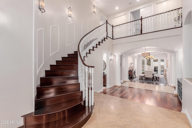 foyer entrance with arched walkways, a towering ceiling, wood finished floors, baseboards, and stairs