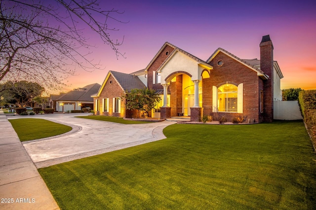 view of front of home with a lawn, a chimney, curved driveway, fence, and brick siding