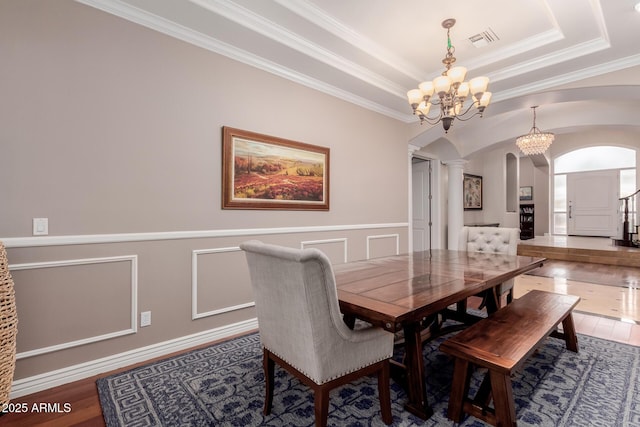 dining area featuring visible vents, arched walkways, a raised ceiling, wainscoting, and wood finished floors