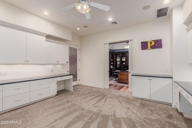 unfurnished office with light carpet, ceiling fan, built in desk, and visible vents