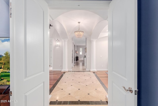 hallway featuring ornate columns, baseboards, arched walkways, and a chandelier