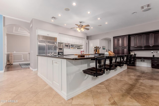 kitchen with arched walkways, dark countertops, visible vents, built in appliances, and a kitchen breakfast bar